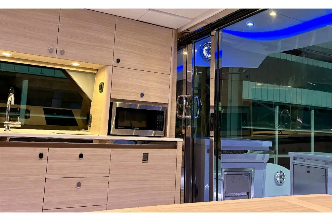 Modern kitchen with wooden cabinetry, stainless steel microwave, and glass doors leading outside; illuminated with LED lights.